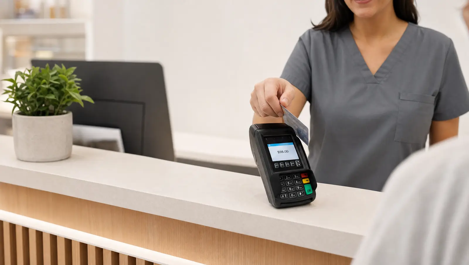 A dental office front desk runs a patient's credit card on a Dejavoo countertop terminal showing a $98 charge.